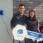 Familia de papá, mamá, niño de 8 años y niño de 4 años están felices de que les estén entregando la llave de su casa, frente a la puerta de entrada de su nueva propiedad.