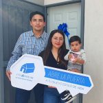 Familia de papá, mamá y niño de 2 años reunidos frente a la puerta de su casa nueva.