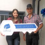 Pareja de adultos jóvenes parados frente a la puerta de su casa nueva, recibiendo las llaves de su casa nueva.