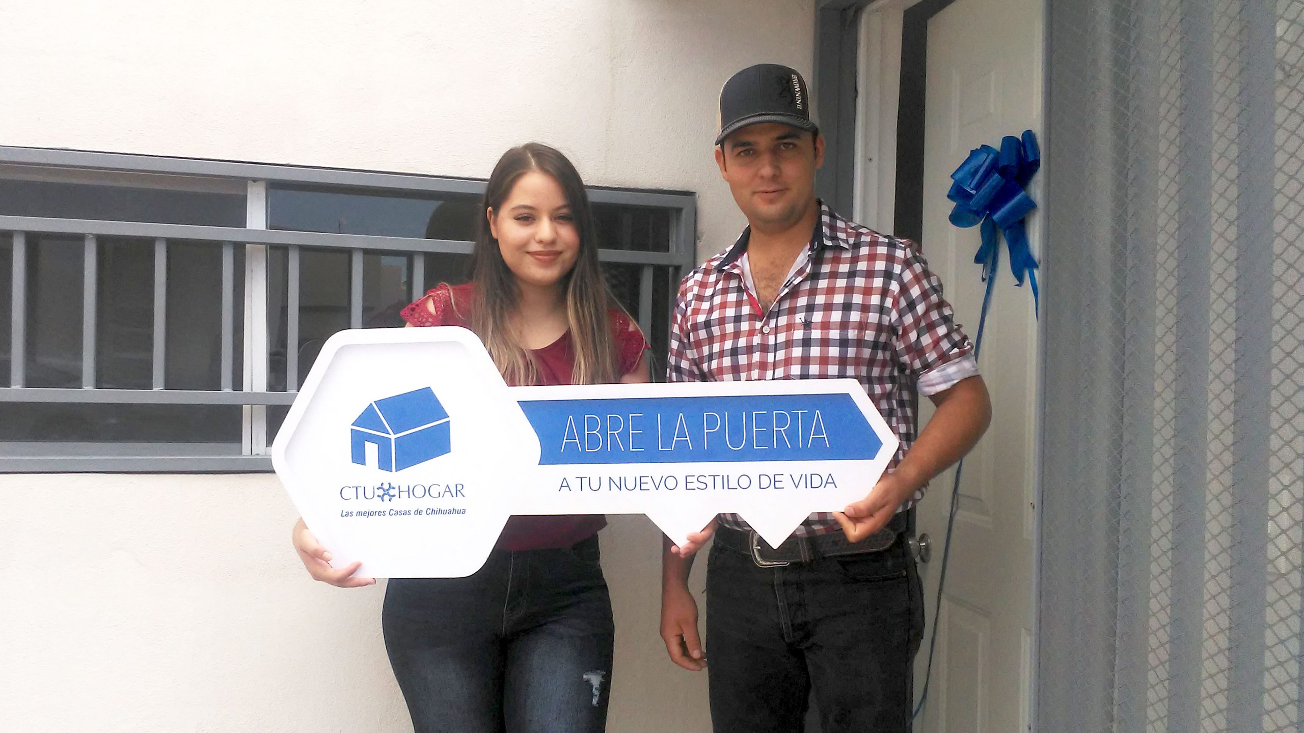 Pareja de adultos jóvenes parados frente a la puerta de su casa nueva, recibiendo las llaves de su casa nueva.