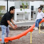 Un padre de familia de cerca de 30 años juega con su hijo de 6 años en un parque mientras su hijo se desliza en un rebaladero.